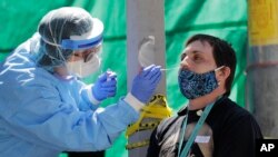 In this May 15, 2020, photo, Tina Nguyen, left, a nurse at at the International Community Health Services clinic in Seattle's International District, takes a nose swab sample from David Carroll, an ICHS employee, during walk- and drive-up testing…