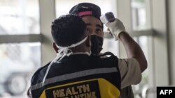 Seorang petugas memeriksa seorang penumpang yang tiba di Bandara Internasional Juanda di Sidoarjo, Jawa Timur, 30 Januari 2020. (Foto: AFP)