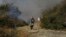 A migrant holds her baby as she runs to avoid a small fire in a field near Mytilene town, on the northeastern island of Lesbos, Greece, Saturday, Sept. 12, 2020. 