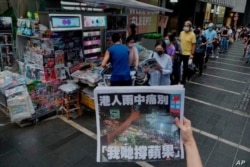Una mujer toma una fotografía de la última edición de Apple Daily mientras la gente hace cola para comprar el periódico en Hong Kong, el 24 de junio de 2021.