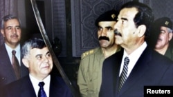 FILE - Former Iraqi president Saddam Hussein examines a sword as he receives SyrianPrime minister Mustapha Miro in 2001.