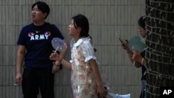 A woman cools herself with a fan as she and her friend walk along a street on a sweltering day in Beijing, Thursday, July 6, 2023.