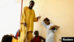 FILE - A girl (R) winces in pain after being hit on the head with a stick by her instructor (C) at a Daraa, or Koranic school, in Pikine on the outskirts of Dakar, May 7, 2008.