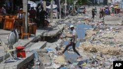 Un hombre cruza un desagüe pluvial lleno de basura en Puerto Príncipe, Haití, el viernes 13 de septiembre de 2024. 