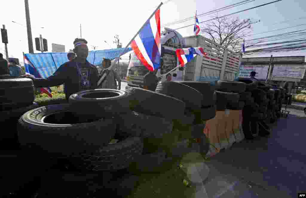 Pengunjuk rasa anti-pemerintah melambai-lambaikan bendera nasional saat memblokir persimpangan jalan dalam unjuk rasa di Bangkok (13/1). (AFP/ Pornchai Kittiwongsakul)