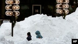 People walk between large piles of plowed snow outside Quincy Market, Jan. 5, 2018, in Boston, following a snowstorm. Forecasters are calling for more bad weather this weekend.