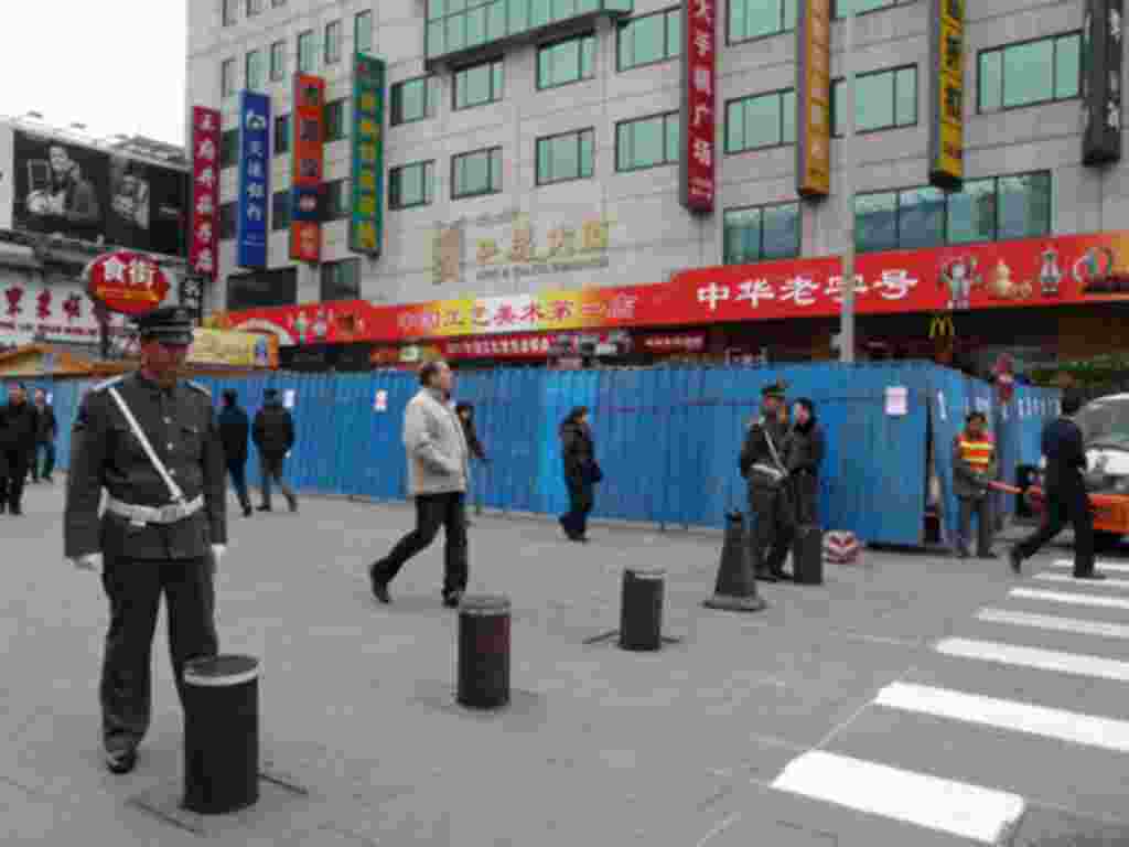 Chinese guards stand at the entrance of the pedestrian Wangfujing area in Beijing. In the background are the blue metal barriers of a construction site that partially blocks the designated spot for anti-government protests, February 25, 2011.