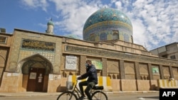 Seorang pria Irak mengendarai sepedanya melewati masjid yang tertutup di tengah restriksi yang diberlakukan pemerintah untuk menekan penyebaran virus COVID-19 di Baghdad, 19 Februari 2021. (Foto: AHMAD AL-RUBAYE / AFP)