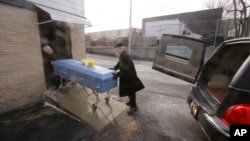Funeral director Paul St. Germaine, left, and driver Richard Derosiers wheel a casket containing the body of 82-year-old James Oram from the Graham Putnam & Mahoney Funeral Parlor to a hearse waiting to take Oram to his final resting place in Worcester, Massachusetts, Feb. 1, 2018.