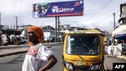 FILE - A woman waits for transport under a campaign billboard for the President of Liberia George Weah in Monrovia, on October 4, 2023.