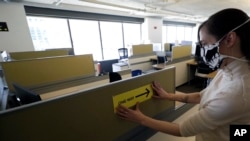 Interior Designer Stephanie Jones at the design firm Bergmeyer puts up a safe distancing reminder indicating one way foot traffic to a cubicle at the firms offices in Boston, Massachusetts, May 7, 2020.