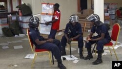 FILE - Zambian police sit at the Civic Center in Lusaka, Zambia, as election volunteers carry ballot boxes, September 22, 2011.