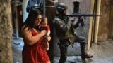 A woman walks with her baby past a PM militarized police soldier in position and aiming his rifle in Rocinha favela in Rio de Janeiro, Brazil on September 23, 2017. 