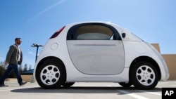 In this May 13, 2015 photo, a reporter walks toward Google's new self-driving prototype car during a demonstration at the Google campus in Mountain View, Calif. 