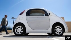 In this May 13, 2015 photo, a reporter walks toward Google's new self-driving prototype car during a demonstration at the Google campus in Mountain View, Calif. 