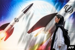 Seorang perempuan berjalan melewati spanduk yang menggambarkan peluncuran rudal yang membawa lambang Republik Islam Iran di pusat Tehran pada 15 April 2024. (Foto: AFP)