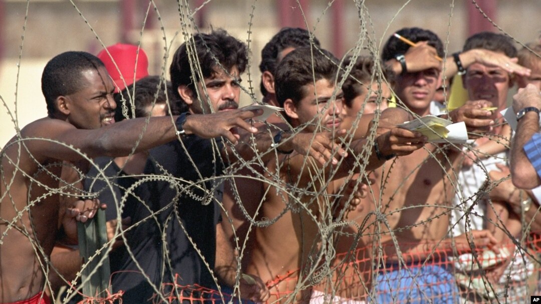 FILE - Cuban refugees hand notes with their names to Navy personnel so that they can get on the list of detainees at the Guantanamo Bay Naval Base in Cuba, Aug. 27, 1994. 