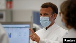 FILE - French President Emmanuel Macron, wearing a protective face mask, gestures as he visits an industrial development laboratory at the French drugmaker's vaccine unit Sanofi Pasteur plant in Marcy-l'Etoile, near Lyon, France, June 16, 2020. 