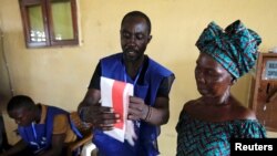 FILE - An election official shows to a woman how to cast her ballot during Liberia's presidential election in Monrovia, Liberia, October 10, 2017.