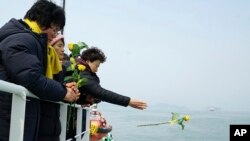 In this photo provided by South Korean Ministry of Oceans and Fisheries, a relative of missing passengers of the sunken Sewol ferry hurls a flower during religious services in waters off Jindo, South Korea, March 28, 2017. 