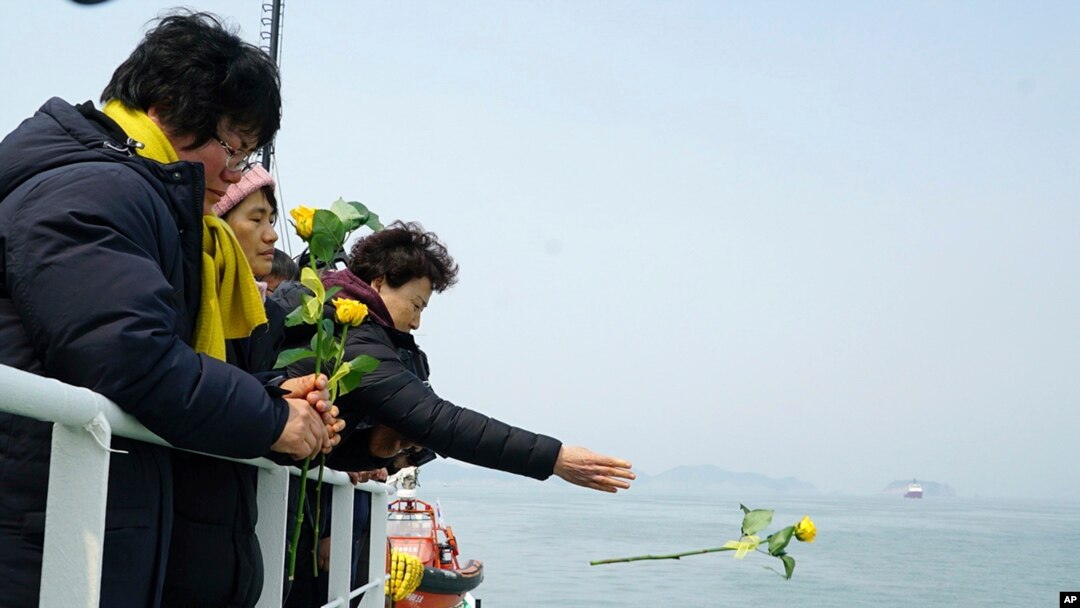 Seorang yang anggota keluarganya termasuk dalam korban yang hilang saat tenggelamnya kapal feri Sewol, melemparkan bunga mawar ke laut Jindo saat diadakan doa bersama untuk mengenang para korban, 28 Maret 2017. (Foto: dok).