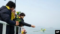 Seorang yang anggota keluarganya termasuk dalam korban yang hilang saat tenggelamnya kapal feri Sewol, melemparkan bunga mawar ke laut Jindo saat diadakan doa bersama untuk mengenang para korban, 28 Maret 2017. (Foto: dok).