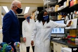 President Joe Biden listens as Kizzmekia Corbett, an immunologist with the Vaccine Research Center at the National Institutes of Health, speaks during a visit at the NIH Feb. 11, 2021, in Bethesda, Md. NIH Director Francis Collins is at center.