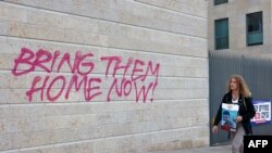 FILE —A woman holding an image of 26-year-old Israeli hostage Ziv Berman walks past graffiti calling for the release of Israeli hostages held in the Gaza Strip since the October 7 attack by Hamas militants in southern Israel, in Jerusalem on November 18, 2023,