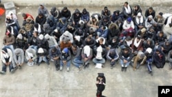 A Carabinieri police officer walks past Tunisian migrants as they wait to board a ship towards Porto Empedocle, in Sicily, where they will be taken for document checks, in Lampedusa, Italy, February 14, 2011