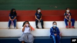 Estudiantes de primer grado, con mascarillas protectoras, se sientan para mantener una distancia social en un gimnasio durante la clase en la escuela técnica San Juan Bautista en Lambare, Paraguay, el miércoles 17 de febrero de 2021.