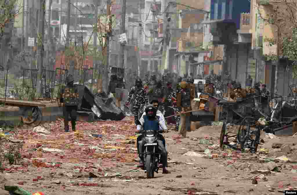 Men ride a motorcycle past security forces patrolling a street in a riot affected area after clashes erupted between people demonstrating for and against a new citizenship law in New Delhi, India.