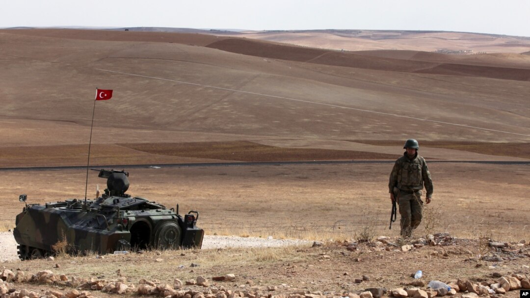 A Turkish soldier stands next to an armored vehicle stationed on a hill top overlooking the fighting positions between Syrian Kurds and Islamic State militants, about 10 kilometers in the west of Kobani in Syria, near Suruc, Turkey, Oct. 2, 2014. 