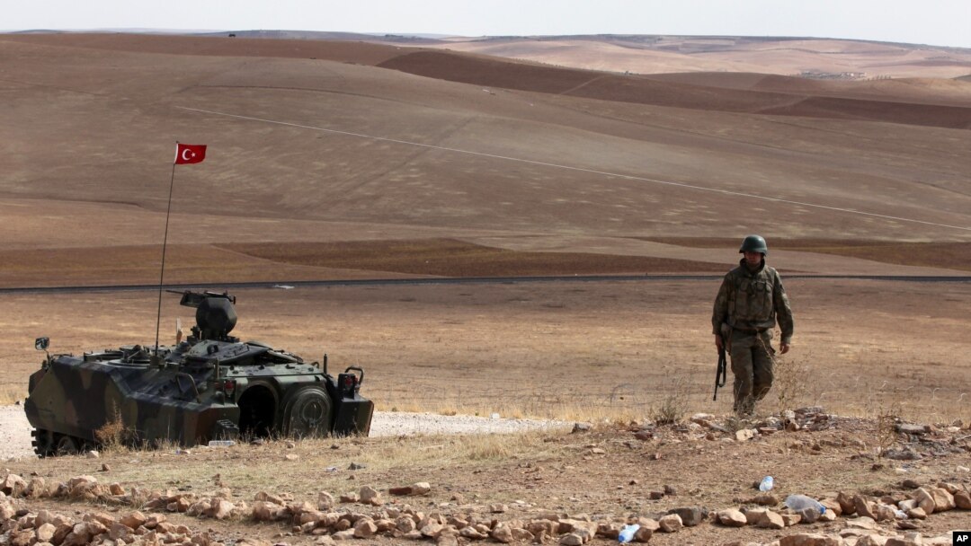A Turkish soldier stands next to an armored vehicle stationed on a hill top overlooking the fighting positions between Syrian Kurds and Islamic State militants, about 10 kilometers in the west of Kobani in Syria, near Suruc, Turkey, Oct. 2, 2014. 