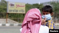 Seorang bocah laki-laki yang memakai masker digendong ayahnya di Taif, Arab Saudi.