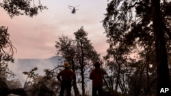 Firefighters watch a water-dropping helicopter while battling the Line Fire in Running Springs, California, Sept. 10, 2024.