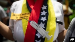 Una enfermera usa una bufanda con colores de la bandera venezolana, y un recorte que representa una jeringuilla, durante una protesta para exigir una distribución más equitativa y rápida de las vacunas, en Caracas, el 17 de abril de 2021. 