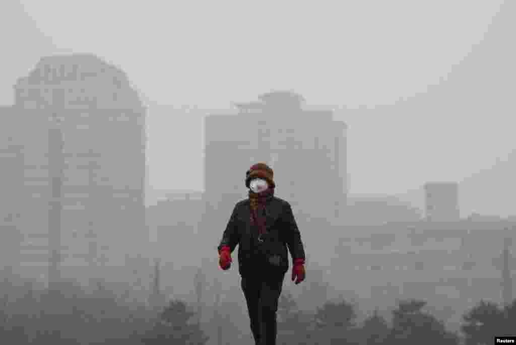 Uma mulher usando uma máscara de protecção passeia num parque de Pequim na manhã de um dia de nível extremo de poluição. China, 8 de Dezembro 2015