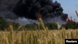 Api dari terbakarnya pabrik pengolahan gas terus berkobar di belakang ladang gandum. Pabrik itu terkena tembakan pasukan Rusia di wilayah Kharkiv, Ukraina, 21 Juni 2022. (Foto: REUTERS /Leah Milis)