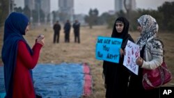 FILE - A Pakistani student uses her mobile phone to take a picture of her friends holding banners prior to a protest in Islamabad, Pakistan, Dec. 19, 2014. Some activists say that the Pakistani government has been silencing critics by selectively reporting their social media posts to platforms like Facebook and Twitter as unacceptable content.