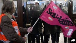 A demonstrator holds a trade union flag as French riot police officers secure the area at the Bordeaux train station, southwest France, Friday Oct. 22, 2010, during a demonstration against President Nicolas Sarkozy's bid to raise the retirement age to 62.