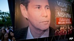 FILE - Women stand beside a poster of late prosecutor Alberto Nisman, marking the first anniversary of his death, in Buenos Aires, Argentina, Jan. 18, 2016.