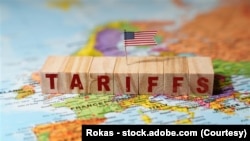 用积木搭成的“关税”(英文)字样摆放在欧洲地图上，上面放着一面美国国旗。