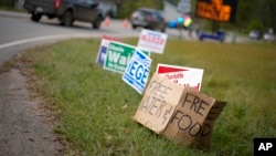 FILE - A makeshift cardboard sign leans up against campaign posters near a relief center on Oct. 3, 2024, in Vilas, N.C., in the aftermath of Hurricane Helene. 