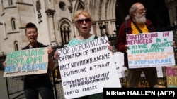 FILE: Demonstrators hold placards as they protest against Britain's Rwanda asylum plan outside the High Court in London. Taken June 13, 2022. 