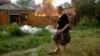 A woman runs from a house that's on fire after shelling in Donetsk, on territory under control of the Donetsk People's Republic, in eastern Ukraine, June 3, 2022.