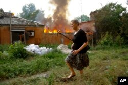 A woman runs from a house that's on fire after shelling in Donetsk, on territory under control of the Donetsk People's Republic, in eastern Ukraine, June 3, 2022.