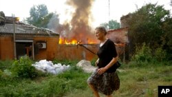 A woman runs from a house that's on fire after shelling in Donetsk, on territory under control of the Donetsk People's Republic, in eastern Ukraine, June 3, 2022.