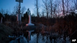 FILE - An international border marker, viewed from the Canadian side of the border near Hemmingford, Quebec, across from Perry Mills, N.Y. (background), is reflected in a small stream at sunset, Feb. 26, 2017. Canada has been increasingly seen as a haven for some immigrants.