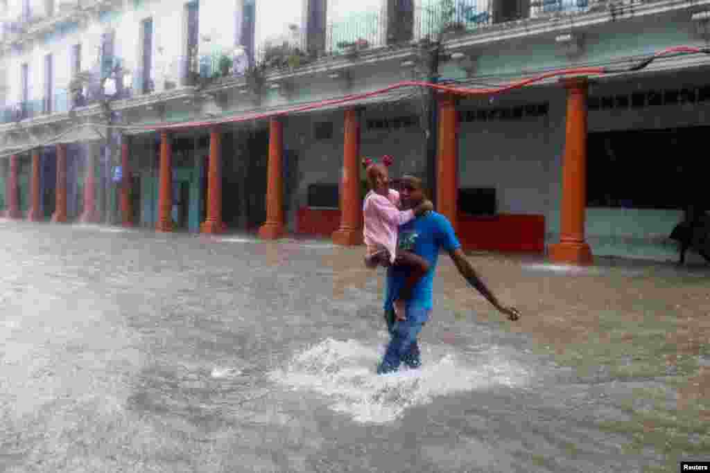 Un hombre carga en sus brazos a una niña y atraviesa una calle de La Habana en medio del aguacero.