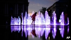 A young girl runs in a public fountain in front of the opera house as the sun sets in Lviv, Ukraine, June 2, 2022.